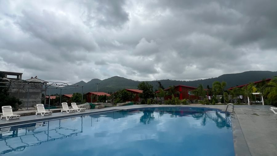Outdoor swimming pool area at Daksh The Valley Resort, Saputara. Wide view of the water and surrounding paved deck.