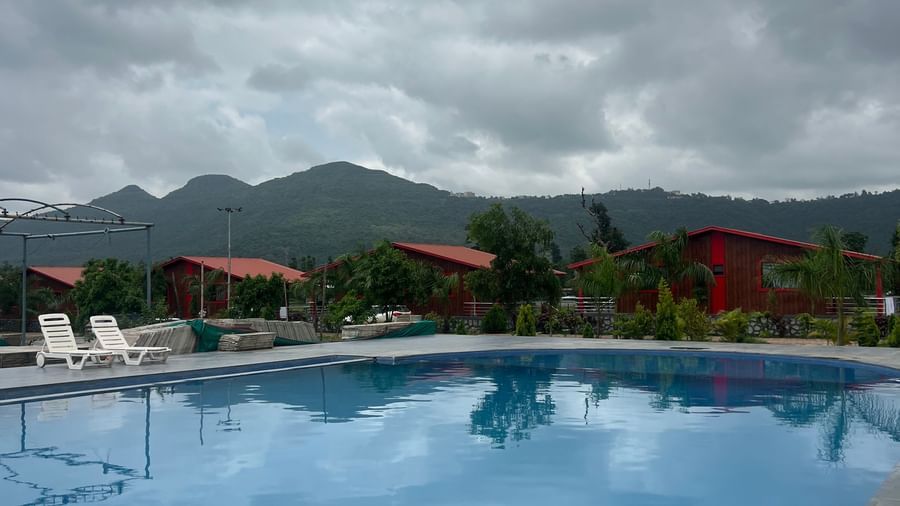 Panoramic scene of the resort swimming pool at Daksh The Valley Resort, Saputara, with water in the pool reflecting the sky and landscape.
