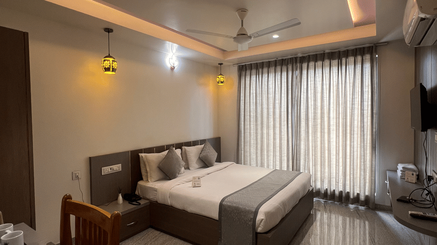 Wide view of the Deluxe Room with Road View at Daksh The Valley Resort, Saputara, showcasing its centrally placed king size bed, closed curtains, warm overhead lighting, and marble flooring.