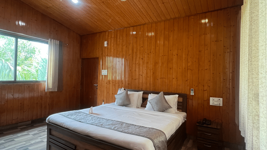 Wide view of the Executive Cottage with Mountain View, highlighting its wooden interiors, a window with curtains opened, and its centrally placed double bed, at Daksh The Valley Resort, Saputara.