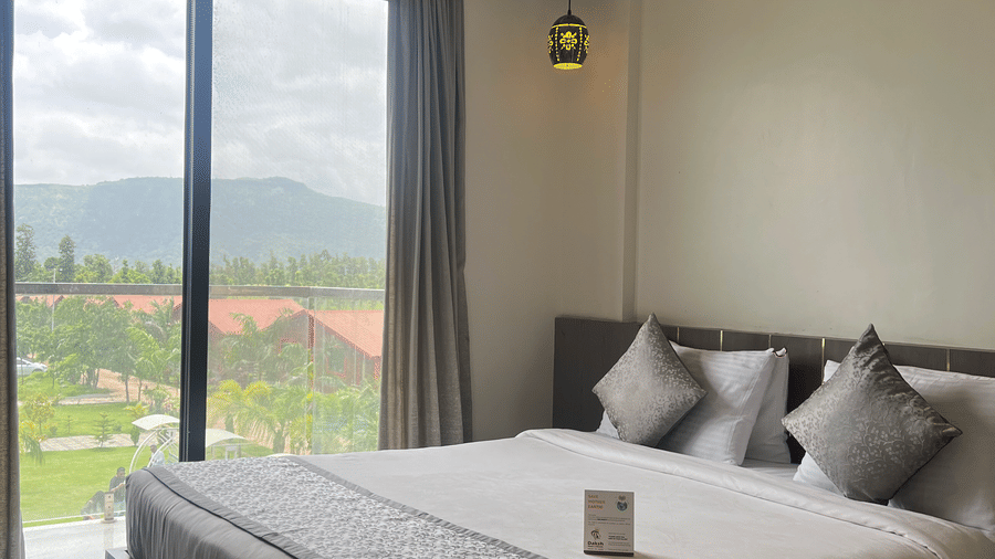 Close up of the queen size bed in the Superior Room with Mountain View at Daksh The Valley Resort, Saputara, with curtains drawn, offering views of the greenery surrounding the room.