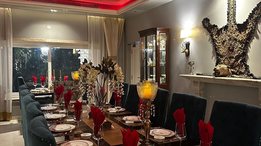 A long dining table set with plates and cutlery, under a red ceiling with neon lighting, in a room with grey walls and decorative wall sconces | Dileep  Kothi, Jaipur