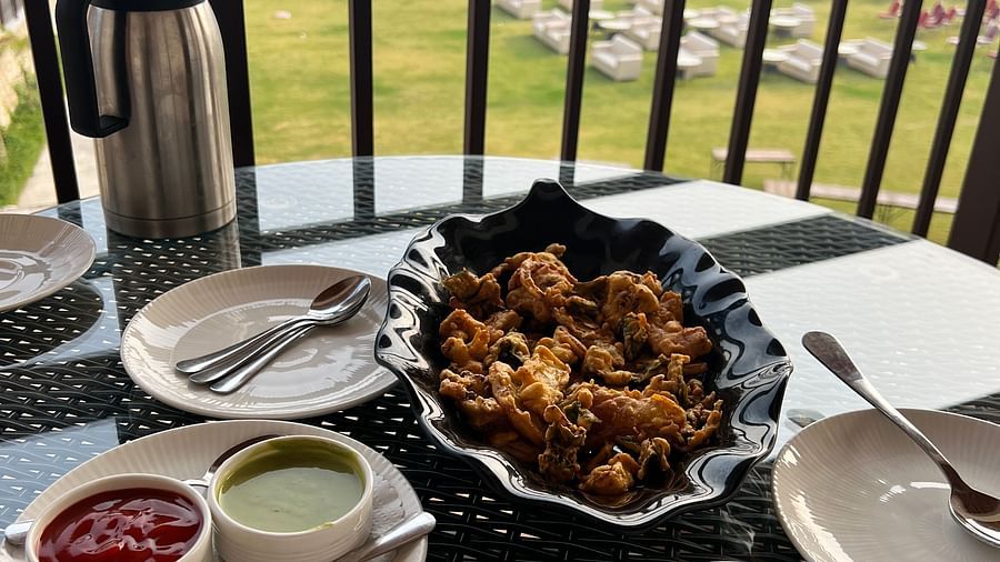 A breakfast spread on a balcony overlooking a golf course, featuring a cup of tea, a plate of crispy fries with dipping sauces, and a water bottle.