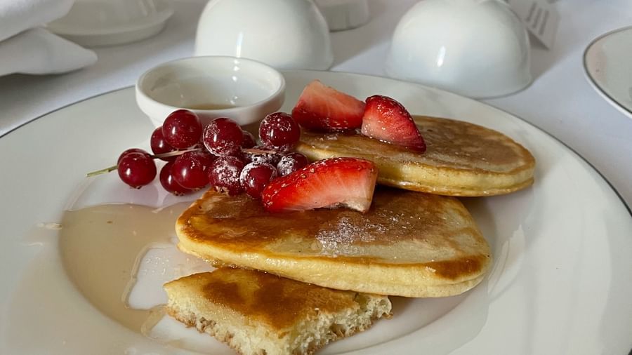 Close-up of a white plate with pancakes topped with strawberries and a glass of juice at Fireflies Resorts, Kabini.
