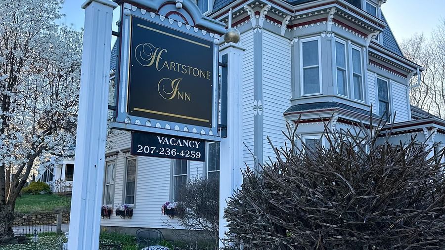 Street-facing view of Hartstone Inn signboard in front of the inn’s Victorian exterior, framed by trees and hedges.