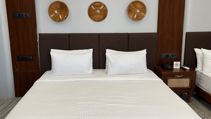 Front view of the double bed with 2 pillows kept against the headboard of the bed and several art pieces wall-mounted above it at Hotel Mumbai House, Pithampur.