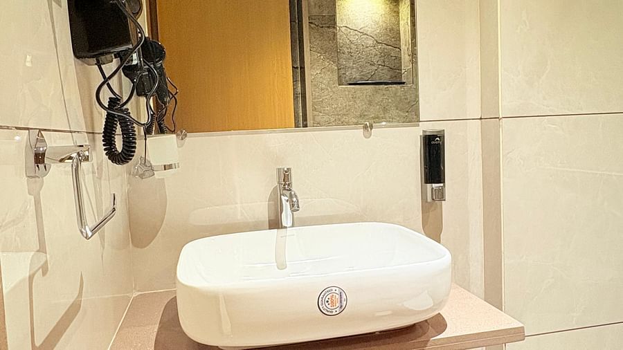 Interior view of a bathroom featuring a wash basin, mirror, and wall-mounted hair dryer at Hotel Mumbai House, Vashi