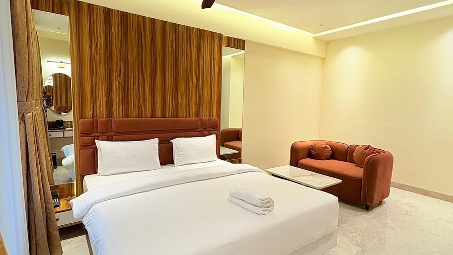 Spacious bedroom with a bed and a sofa placed next to it, offering a seating area at Hotel Mumbai House, Vashi.