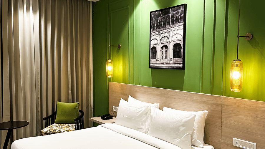 A hotel room with a large comfortable bed, wall lamps attached near the head bed and a painting on a green wall - Wonder Hills