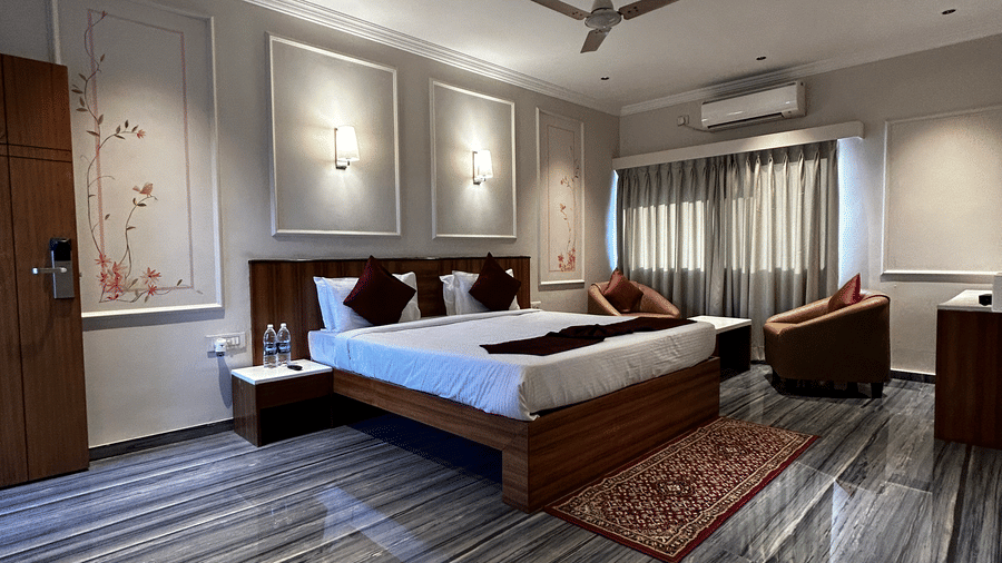  A spacious hotel suite with polished grey marbled flooring, a wooden bed, and a separate seating area at Pravasa Hotel, Kolhapur. 