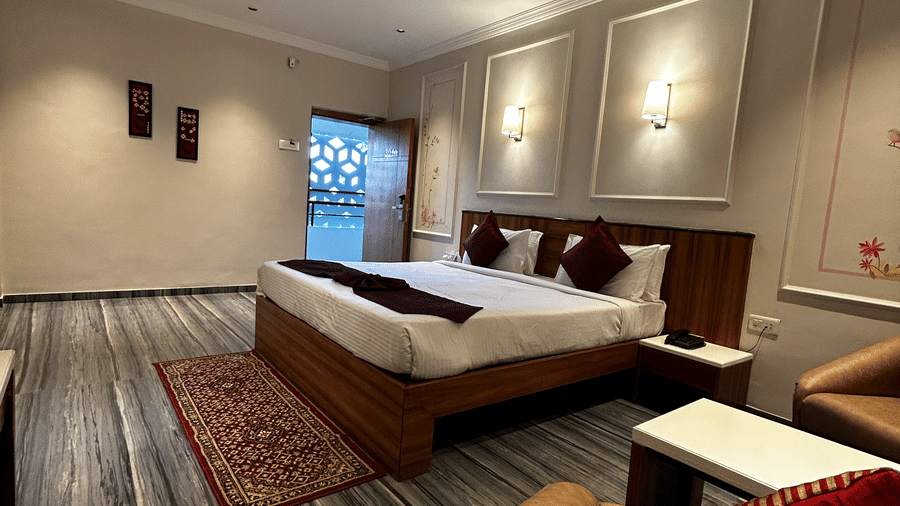 A comfortable hotel room featuring a double bed, tan armchair seating, and grey marble-effect flooring at Pravasa Hotel, Kolhapur.