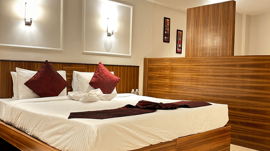 A contemporary double bedroom with a wooden headboard, red throw pillows, and a partial wooden room divider at Pravasa Hotel, Kolhapur.