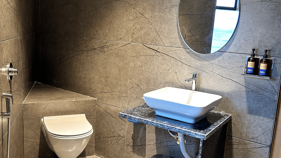A contemporary washroom with slate-grey tiled walls, a vessel sink, and a modern circular mirror at Pravasa Hotel, Kolhapur.