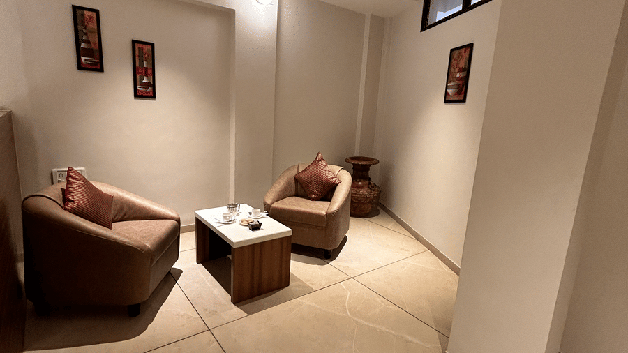 A simple and private meeting or waiting area with two curved chairs and a small dark wood table at Pravasa Hotel, Kolhapur.
