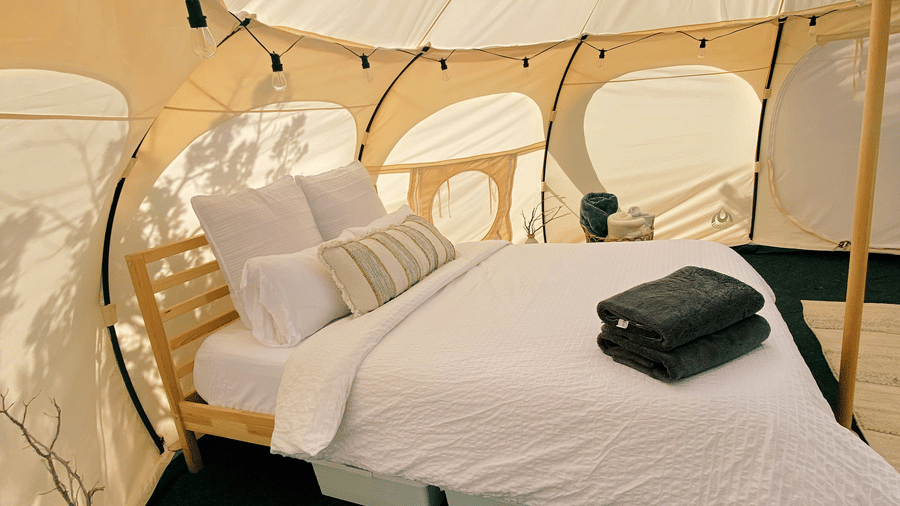 The interior of a modern glamping tent with a bed, chairs, and a window in the ceiling to view the sky.