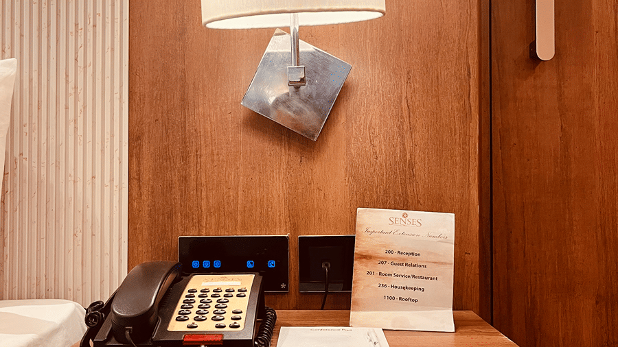 The bedside table at the Premier Smart Suite with a lamp mounted on the wall along with a telephone on the table.