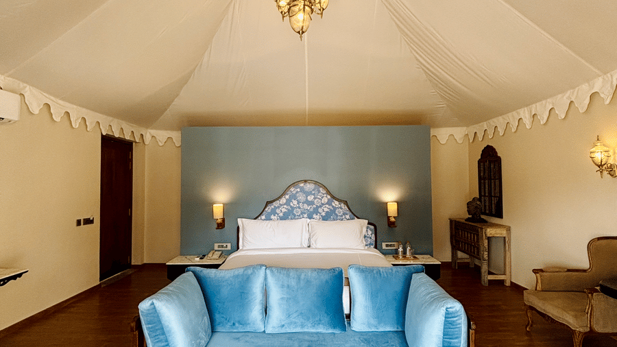 Vana Junior Suite in Surpura Bagh featuring  king size bed, bedside table and lamps on either side, a long sofa, two sofa chairs with centre table, and a table with antique piece at one corner.