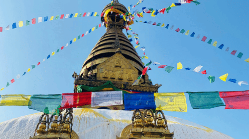 A golden stupa with colourful prayer flags strung across it, set against a bright blue sky.