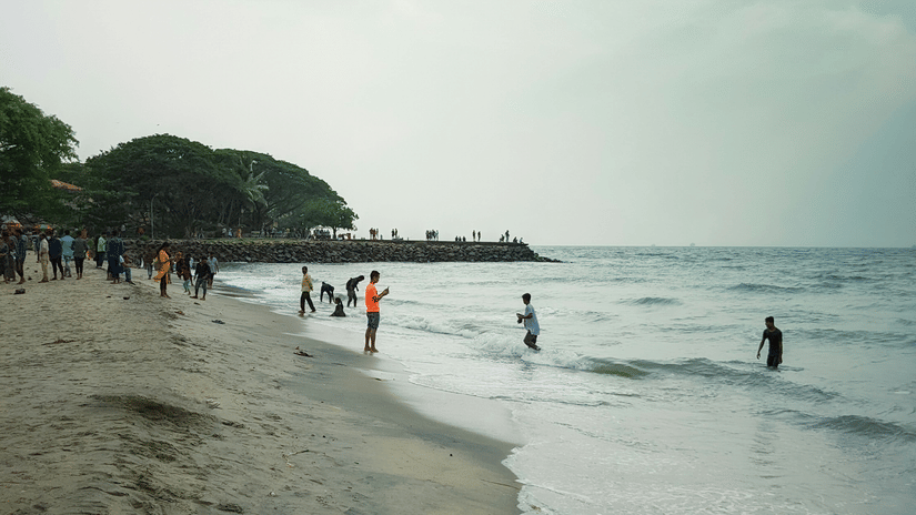 Sandy Fort Kochi beach stretching along calm waters, with visitors wading in the sea
