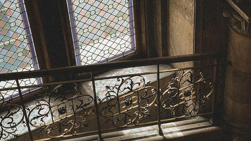 An upward-looking indoor shot of intricate, arched architecture with stained glass windows and ornate railings, possibly in an old building or palace.