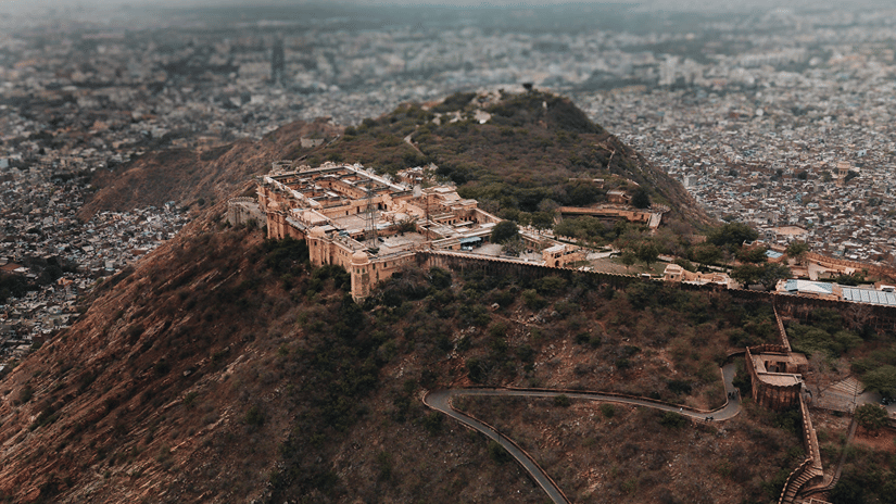 An ancient hilltop fort overlooks a sprawling city spread across the valley beneath a hazy sky.
