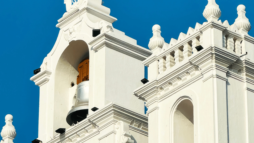 The crisp white facade of a historic colonial church stands out strikingly against a clear blue sky.