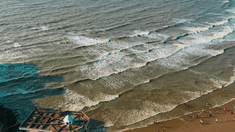 An aerial shot of a beach with people enjoying the waves beside a watch tower