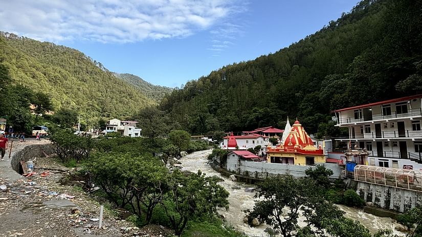 A view of a temple nestled in a valley surrounded by mountains,flowing river, with a clear blue sky and fluffy clouds.