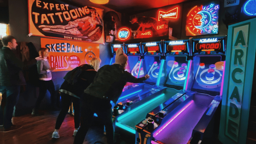 An overview of an arcade place with two guys playing games on the neon-lit machines.