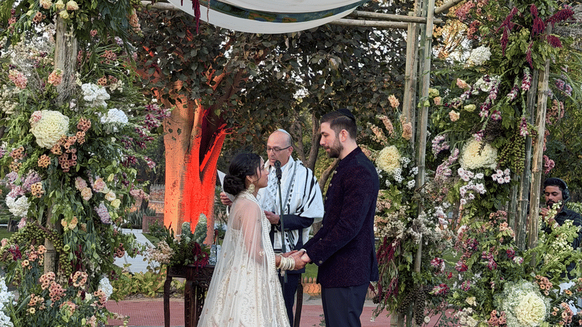 A bride and groom standing before a beautifully decorated outdoor floral altar with candles lining the aisle at Umaid Palace.