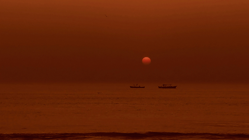 One of the beach in Jamnagar with the golden sun hovering above the calm sea at dusk, casting warm amber tones across gentle waves beneath a clear evening sky