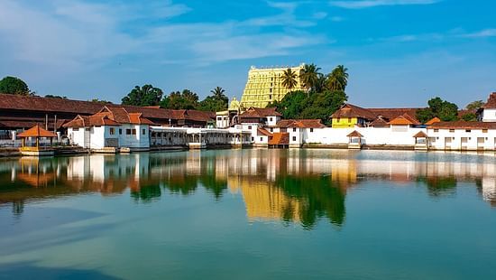 The Sree Padmanabhaswamy Temple in Thiruvananthapuram is reflected in the still waters of a surrounding pond under a clear blue sky.