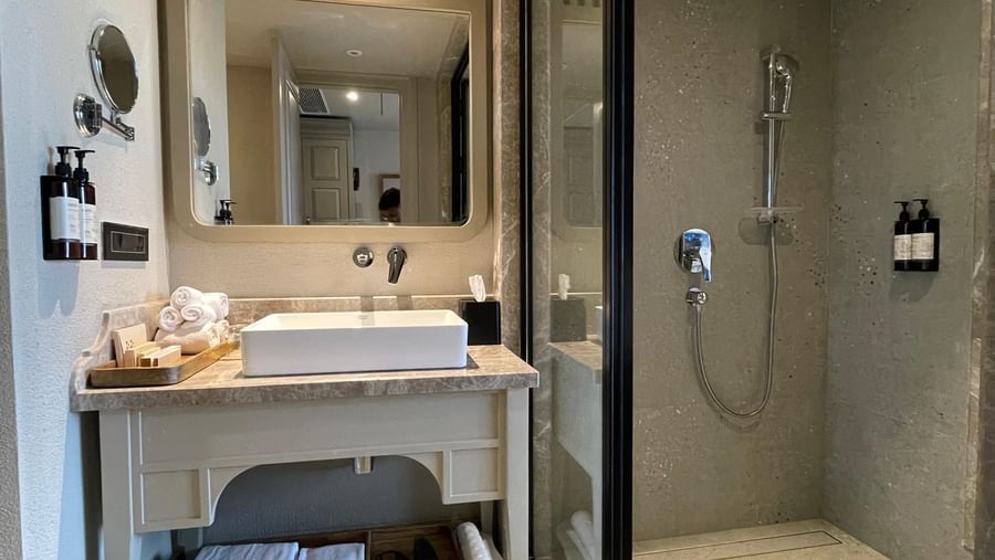A detailed shot of the vanity and shower area in a guest bathroom at The Evren, Vagator. The vanity has a clean, white vessel sink, and the walk-in shower is separated by a clear glass panel.