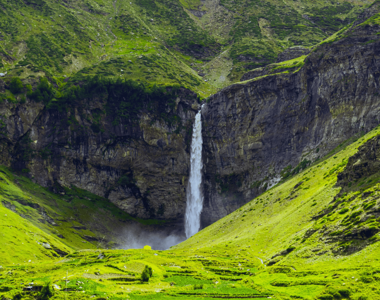 A far out view of a waterfall in a forested area with greenery all around.