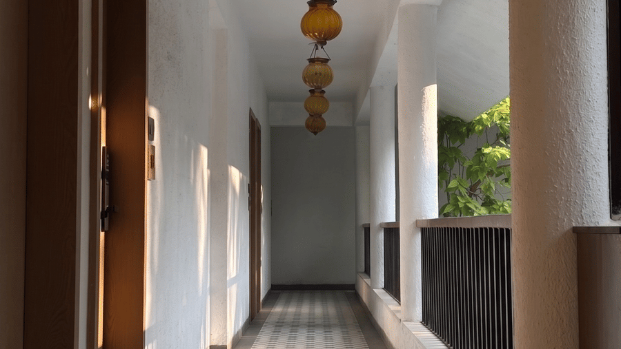 Hanging lamps, patterned floor tiles, and a wooden railing line a long corridor at Bougainvillea, Alibaug.