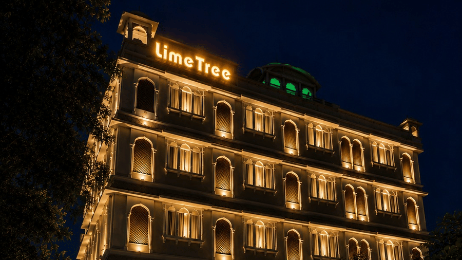 Night view of the entrance and illuminated exterior building of Lime Tree Hotel & Banquet, Jaipur, with cars parked out front.