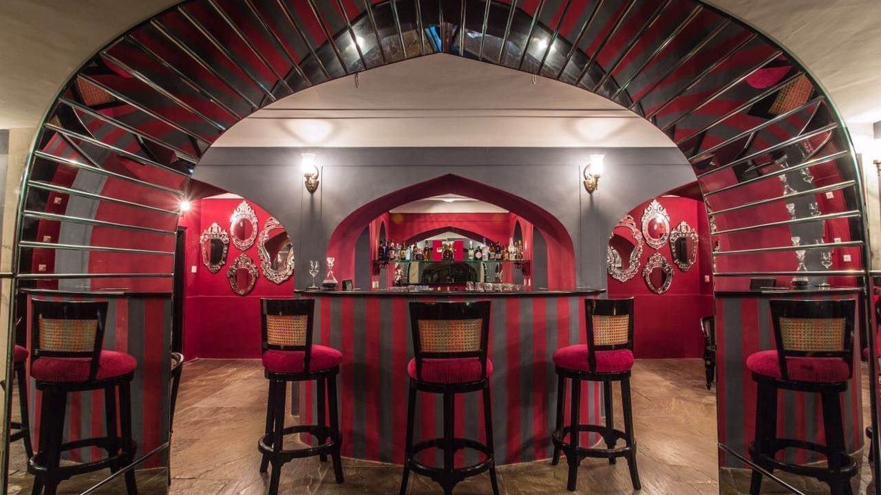 A bar area at Royal Heritage Haveli featuring red walls, arched architectural details, and bar stools.