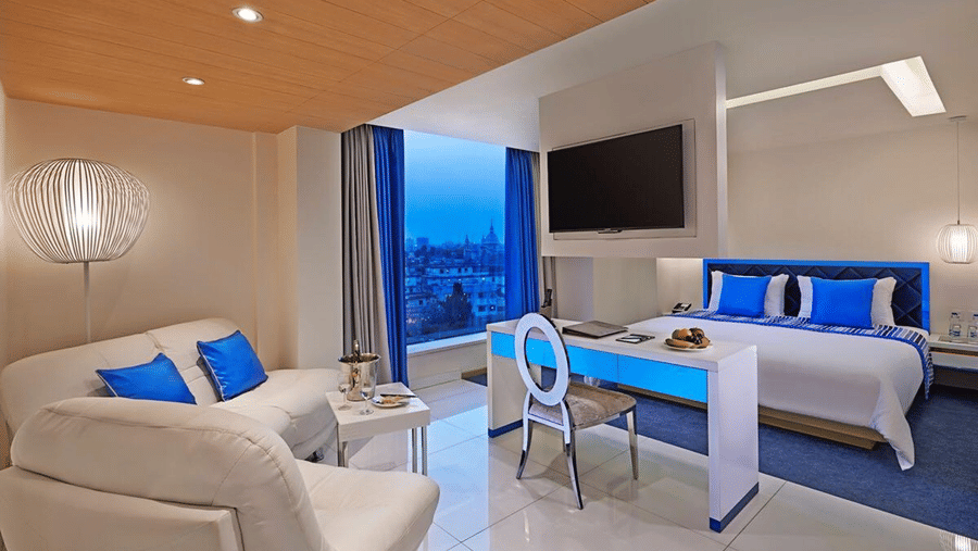 A Superior Room at Barsana Boutique Hotel, Kolkata, featuring a modern couch and a plush bed placed next to a large window offering city views from the room.