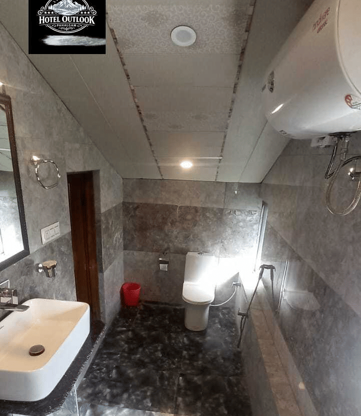 A bathroom at Hotel Outlook, Pahalgam, with patterned stone walls, a rectangular mirror, a dark counter sink basin, and a glass shower cubicle.