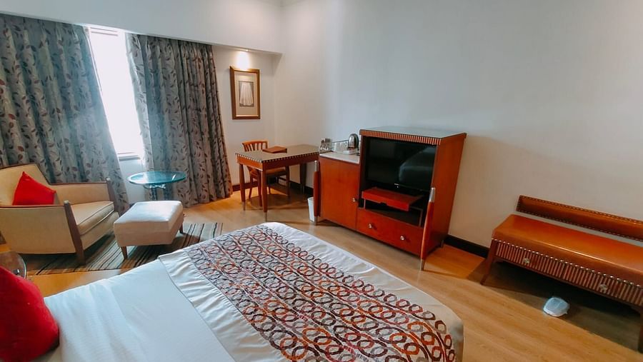 A bright hotel room featuring a king size bed, wooden furniture and red accent pillows, creating a warm and inviting ambience – Hotel Hindusthan International, Kolkata