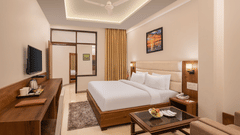 Premium Suite Room at Pride Ashiyana Resort Mussoorie featuring a plush bed facing the TV mounted on the wall and a coffee table with a couch next to it