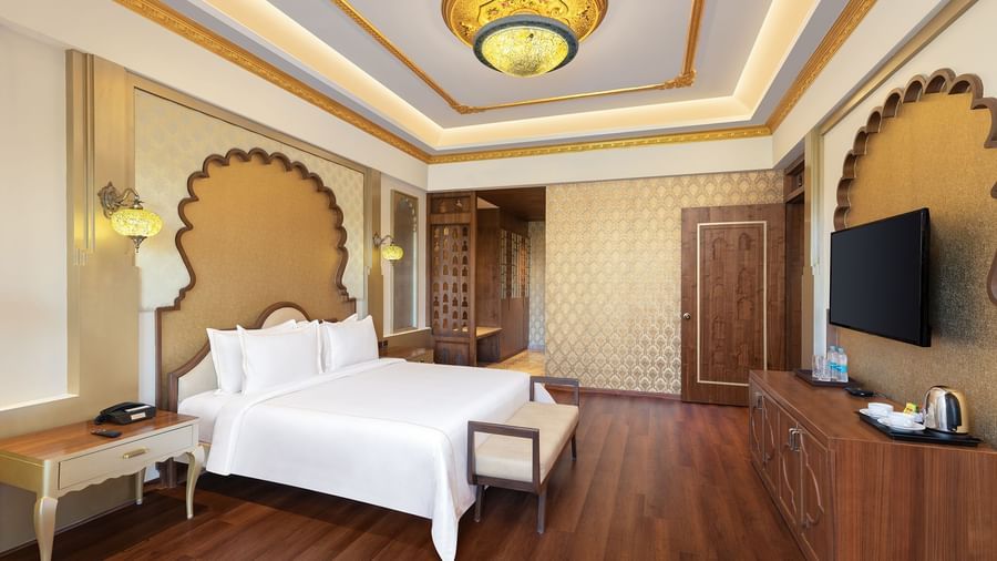 A sophisticated bedroom with wooden floors, golden accents, and plush white bedding – Kaldan Samudra, one of the finest luxury hotels in Mahabalipuram