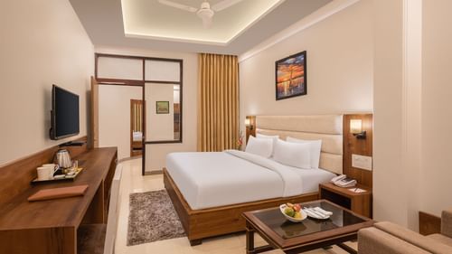 Premium Suite Room at Pride Ashiyana Resort Mussoorie featuring a plush bed facing the TV mounted on the wall and a coffee table with a couch next to it