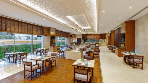 Cafe Pride at Pride Plaza Hotel, New Delhi featuring different types of accommodation and a view of outside because of blinds drawn on one side of the dining space.