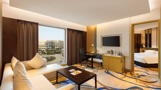 Premium Luxury Suite at Pride Plaza Hotel, New Delhi featuring the living room where a sofa set is placed in front of a TV along with a coffee table and the bedroom is seen from a corner