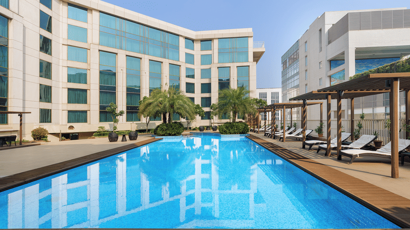 Swimming pool surrounded by trees and buildings of Pride Plaza Hotel in New Delhi.