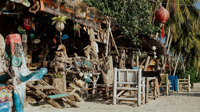 A rustic beachside shop with handcrafted souvenirs and seating under a thatched roof, suggesting a relaxed, tropical atmosphere.