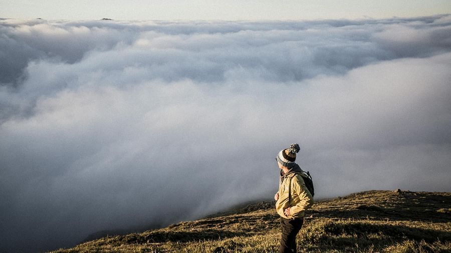 Image of a person standing on a mountain top overlooking a thick blanket of clouds - The Dukes Retreat, Khandala