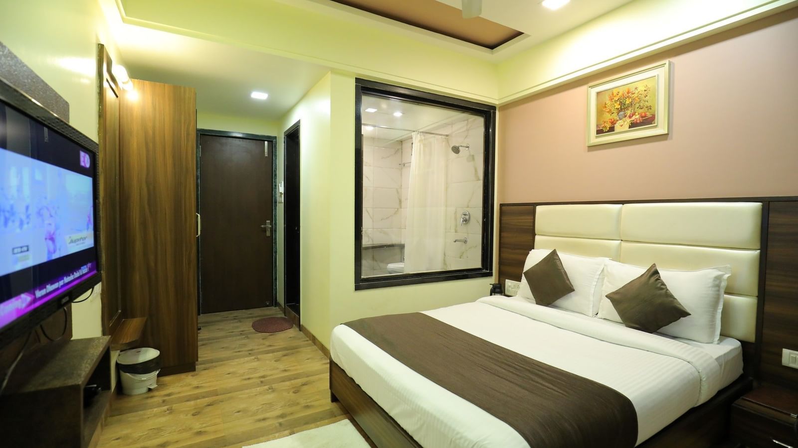 A bedroom at Krushnai Resort with a large TV, a king size bed, and a partial view of the bathroom through a glass wall.