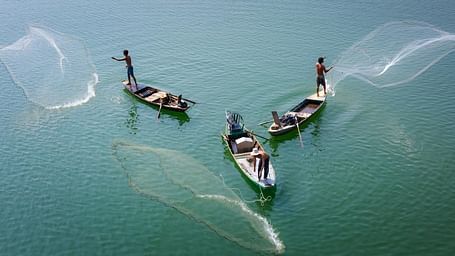 Aerial view of three boats with fishermen on it casting out their net to fish
